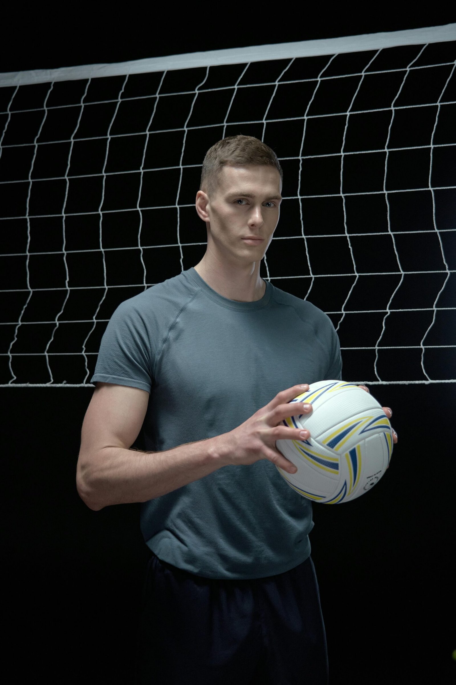 Portrait of a male volleyball player holding a ball in front of a net in a studio setting.